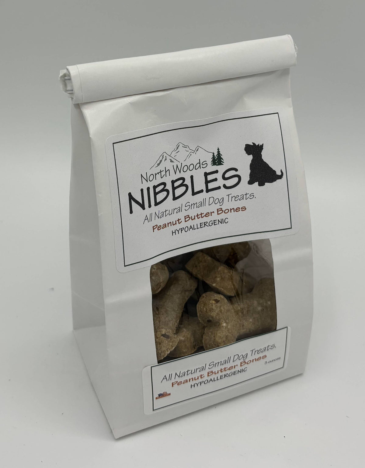 A white stand-up bag of North Woods Nibbles hypoallergenic peanut butter bones dog treats, featuring a clear window showing the brown bone-shaped treats inside.