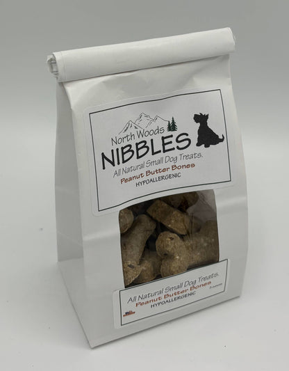 A white stand-up bag of North Woods Nibbles hypoallergenic peanut butter bones dog treats, featuring a clear window showing the brown bone-shaped treats inside.