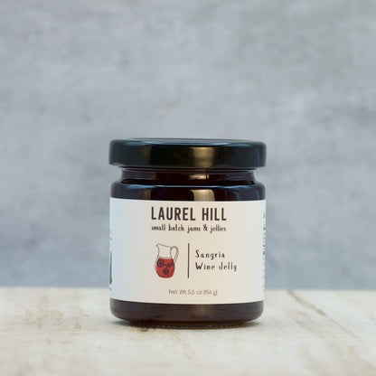 A jar of Laurel Hill Sangria Wine Jelly on a light wood surface against a textured gray background.