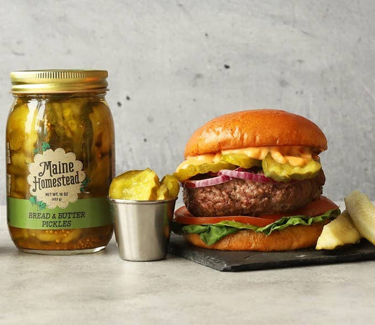 Burger with pickles and a jar of Maine Homestead pickles on a gray surface