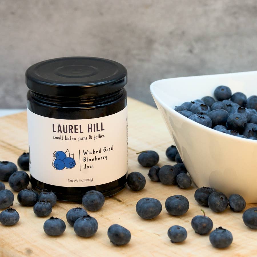 Jar of Laurel Hill Wicked Good Blueberry Jam with blueberries on a wooden surface