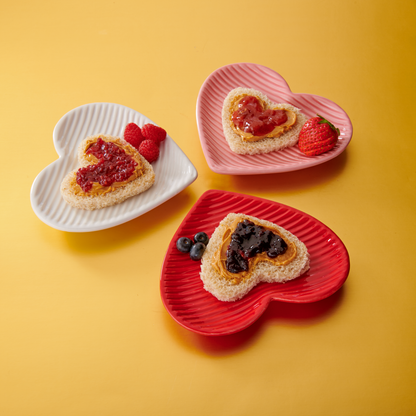 Heart-shaped sandwiches on colorful plates against a yellow background