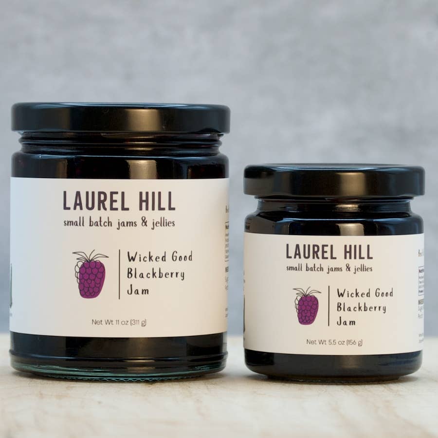 Two jars of Laurel Hill Wicked Good Blackberry Jam on a marble surface with a gray background.