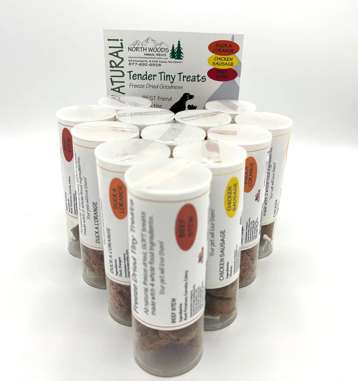 A group of clear plastic treat jars filled with small brown treats, arranged in front of a branded North Woods Pet Supplies card on a white studio background.