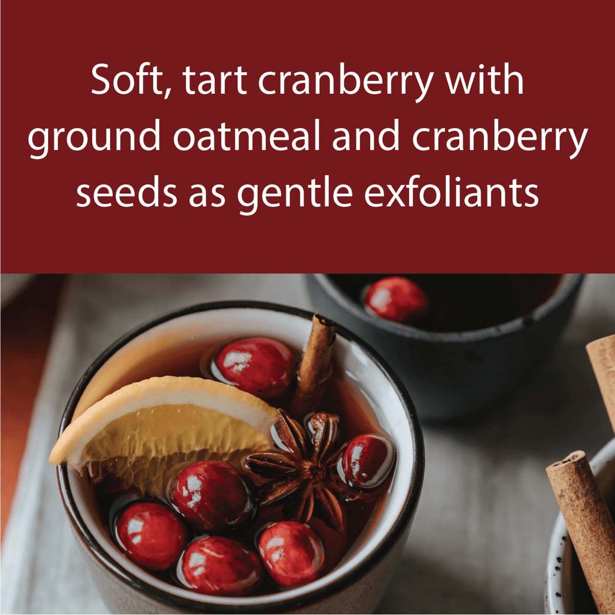 A promotional graphic with a dark red banner containing white text that reads 'Soft, tart cranberry with ground oatmeal and cranberry seeds as gentle exfoliants' above a styled photo of cranberry tea in a ceramic cup, garnished with a cranberry slice, cinnamon stick, and star anise.