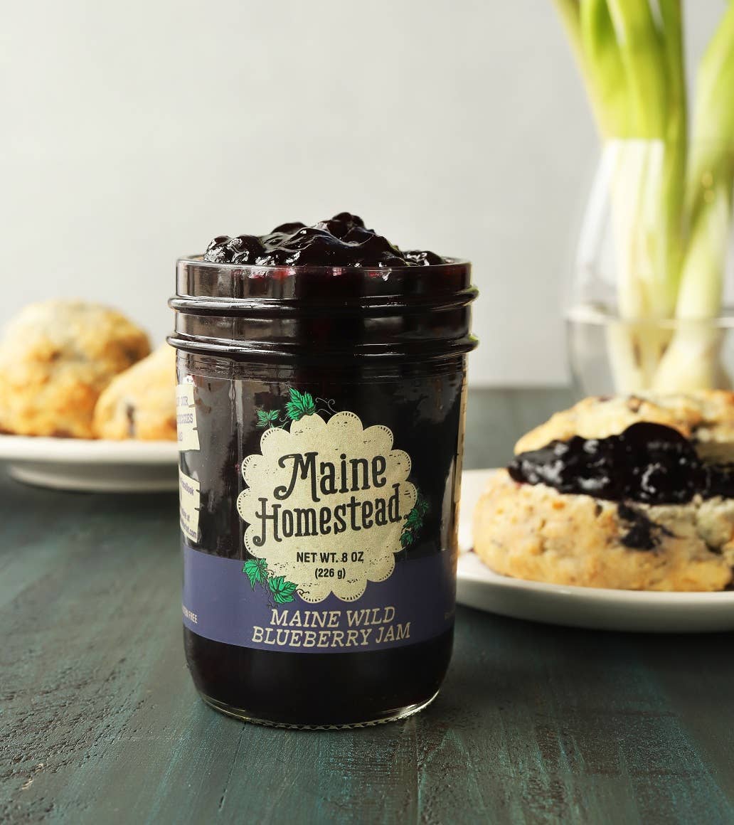 Jar of Maine Homestead blueberry jam on a table with scones in the background