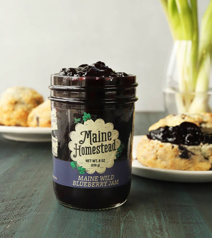 Jar of Maine Homestead blueberry jam on a table with scones in the background