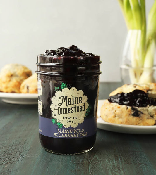 Jar of Maine Homestead blueberry jam on a table with scones in the background