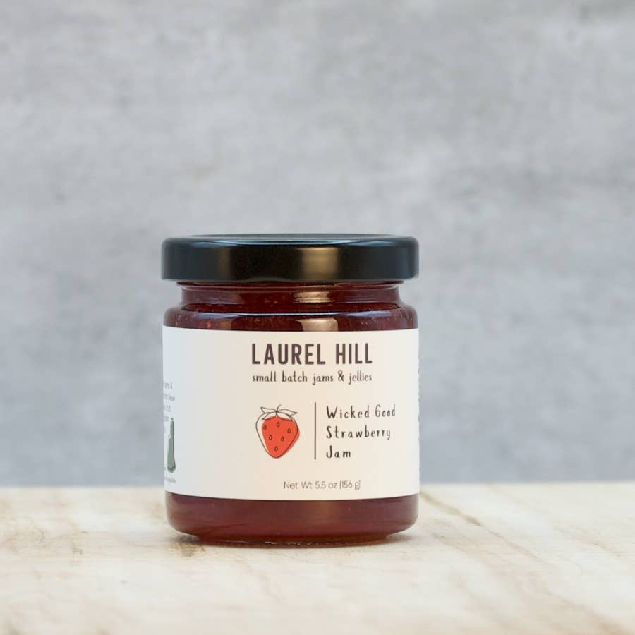Jar of Laurel Hill Wicked Good Strawberry Jam on a wooden surface with a gray background