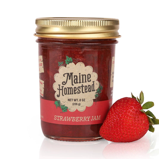 Jar of Maine Homestead Strawberry Jam with a gold lid and a strawberry on a white background