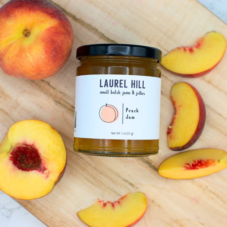 Jar of Laurel Hill Peach Jam surrounded by peaches and slices on a wooden surface