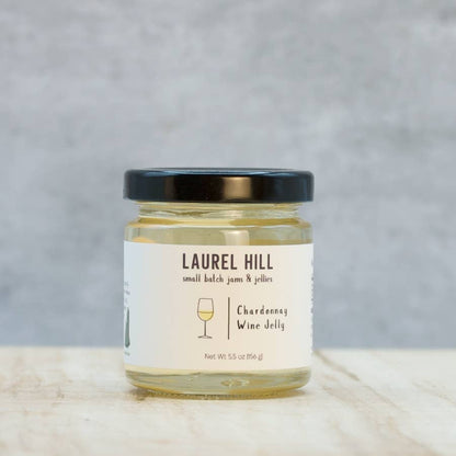 A jar of Laurel Hill Small Batch Jams & Pickles Chardonnay Wine Jelly, featuring a white label and a black lid, set on a light marble surface against a textured gray background.