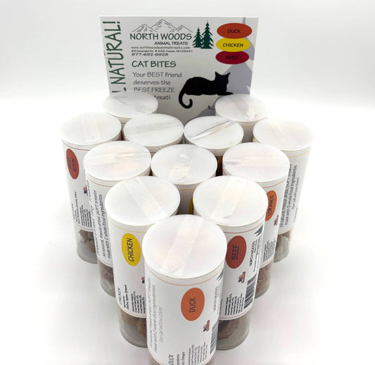 A group of North Woods Animal Treats cat bite containers arranged in a circle, with the product box standing behind them on a white background.