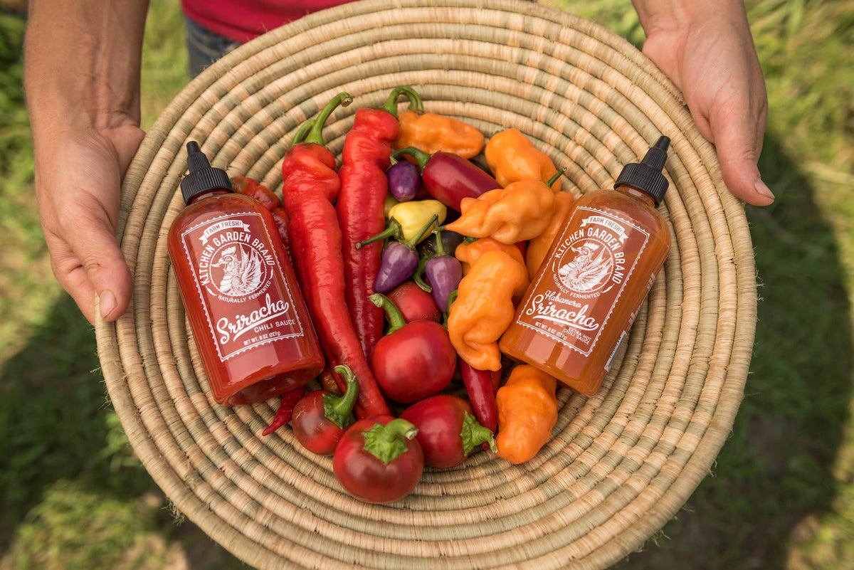 Two bottles of Tabasco sauce on a woven plate with colorful peppers.
