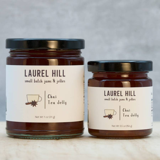 Two glass jars of Laurel Hill Chai Tea Jelly with black lids and cream labels, displayed on a light marble surface against a neutral gray background.