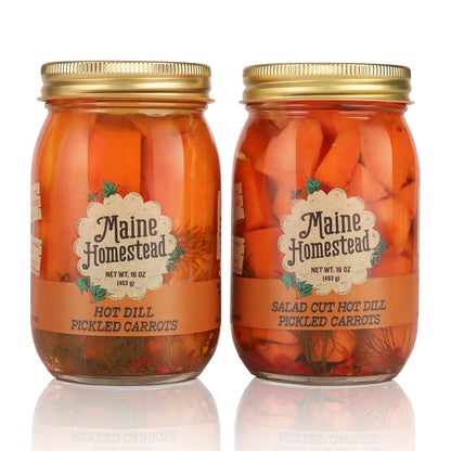 Two glass jars of Maine Homestead pickled carrots with gold lids, one labeled Hot Dill Pickled Carrots and the other Salad Cut Hot Dill Pickled Carrots, on a white background with a reflection.