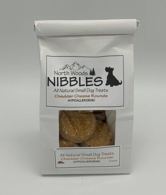 A white stand-up bag of North Woods Nibbles hypoallergenic cheddar cheese round dog treats, featuring a clear window showing the round treats inside.