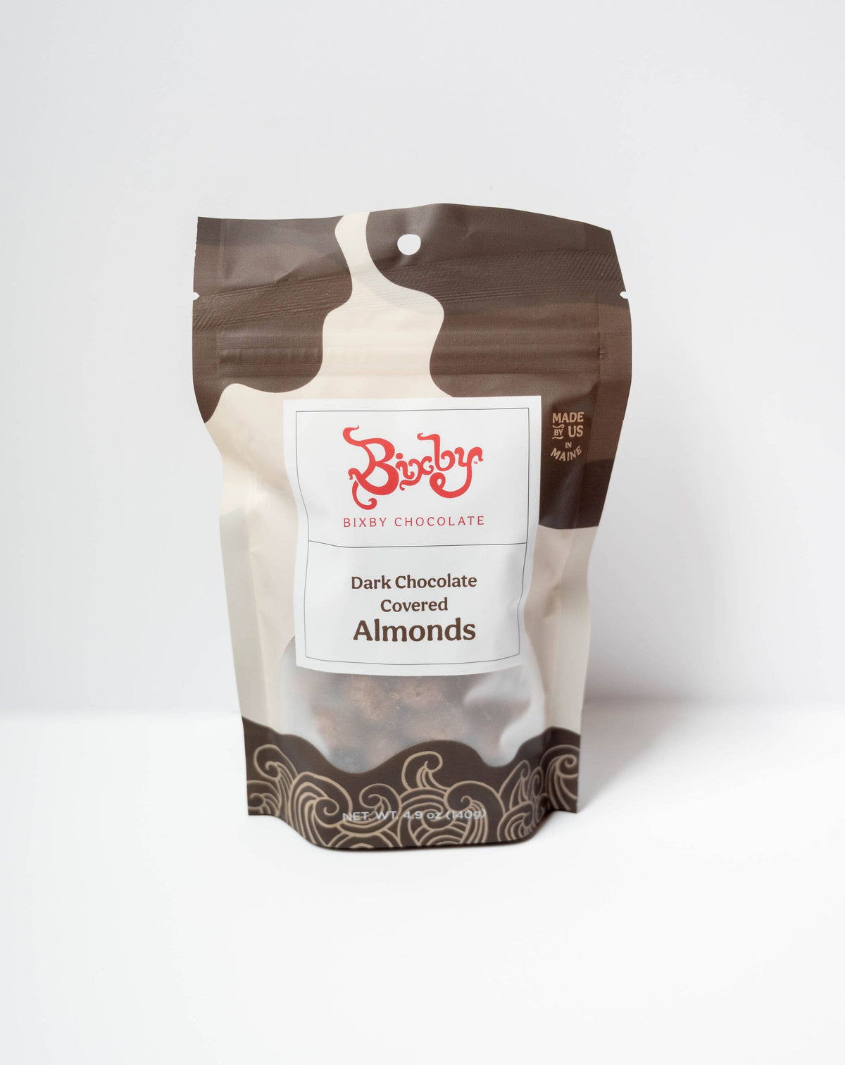 A stand-up pouch of Rixi Chocolate Dark Chocolate Covered Almonds, featuring a brown and beige milk-chip splash design with a white label in the center.