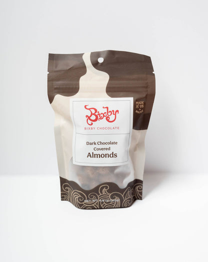 A stand-up pouch of Rixi Chocolate Dark Chocolate Covered Almonds, featuring a brown and beige milk-chip splash design with a white label in the center.