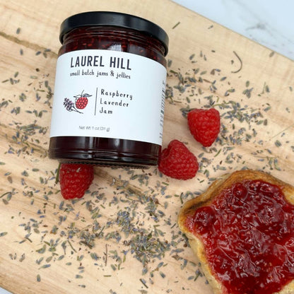Jar of Laurel Hill raspberry lavender jam on a wooden board with raspberries and lavender.