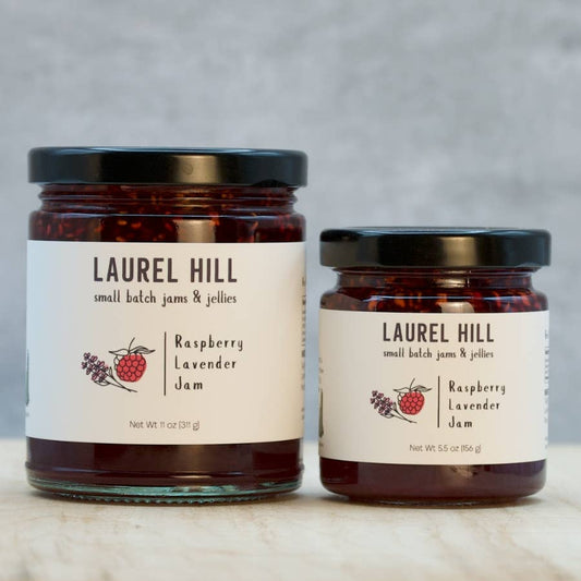 Two jars of Laurel Hill raspberry lavender jam on a wooden surface with a gray background.