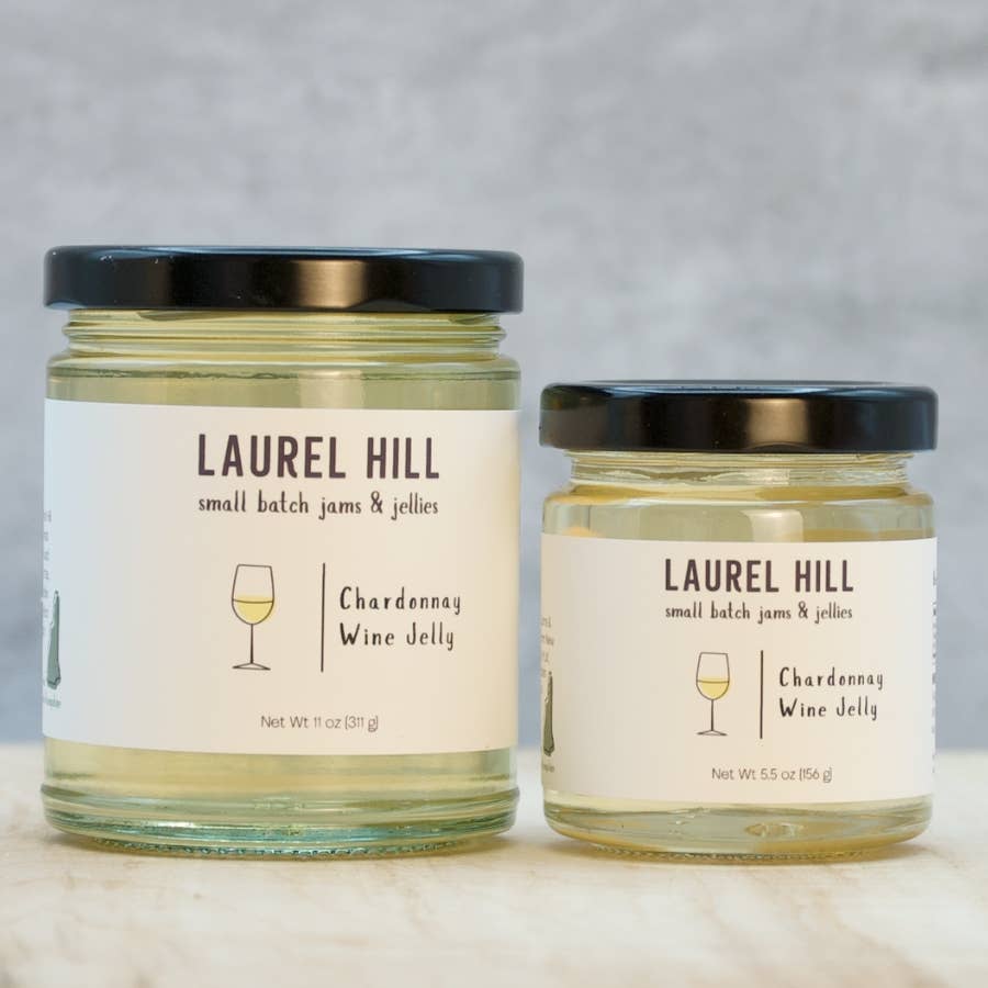Two glass jars of Laurel Hill Small Batch Jams & Jellies, one large and one small, both containing Chardonnay Wine Jelly with cream labels and black lids, set on a light marble surface against a gray textured background.
