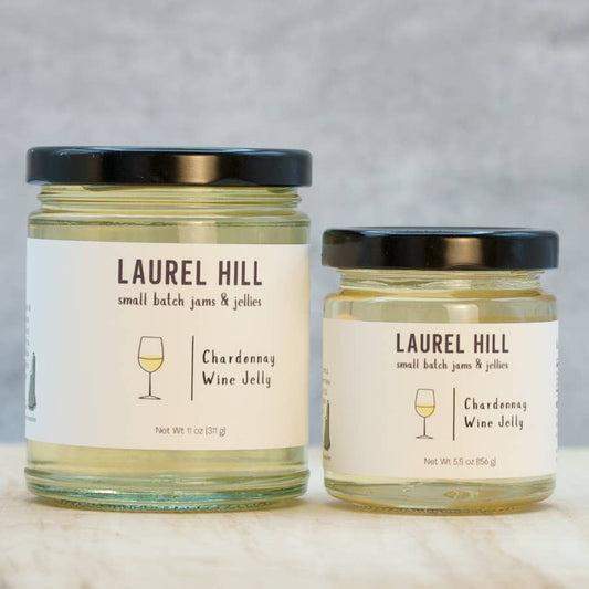 Two glass jars of Laurel Hill Small Batch Jams & Jellies, one large and one small, both containing Chardonnay Wine Jelly with cream labels and black lids, set on a light marble surface against a gray textured background.