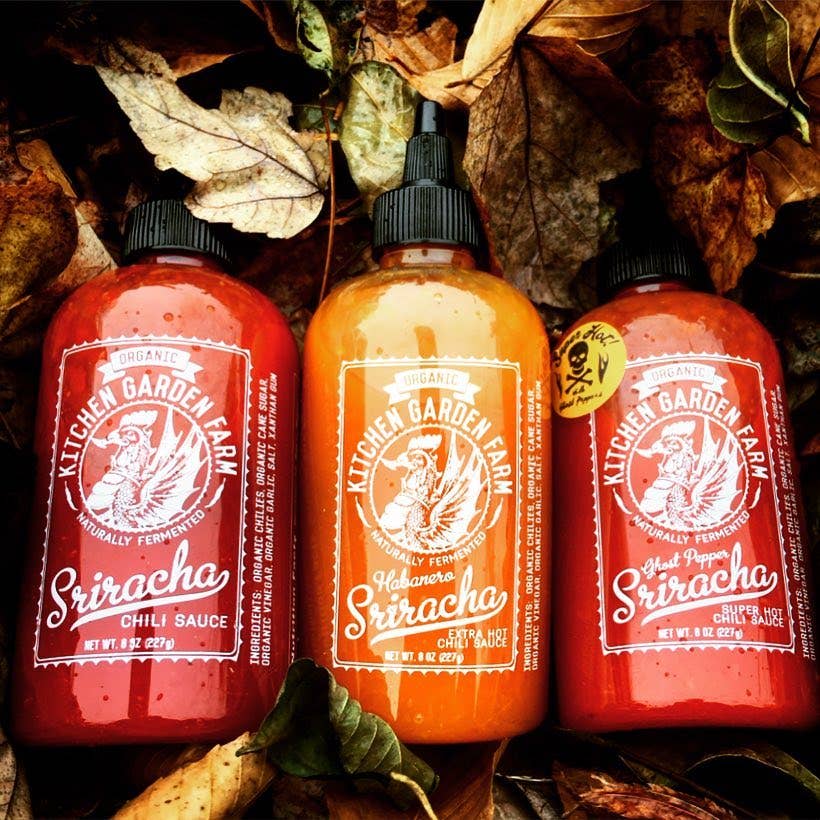 Three bottles of Kitchen Garden Farm Sriracha chili sauce on a leafy background