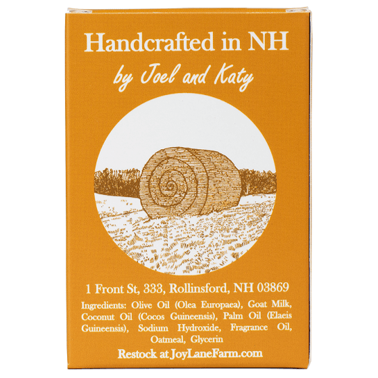 A square orange-brown product box with white text reading 'Handcrafted in NH by Joel and Katy' and a circular illustration of a hay bale in a field. Smaller text lists ingredients and provides JoyLaneFarm.