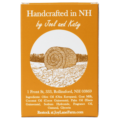 A square orange-brown product box with white text reading 'Handcrafted in NH by Joel and Katy' and a circular illustration of a hay bale in a field. Smaller text lists ingredients and provides JoyLaneFarm.