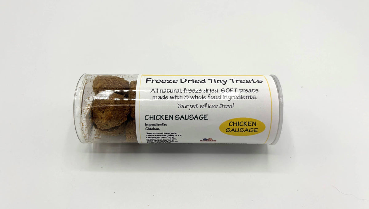 A clear plastic cylinder container of freeze dried tiny treats, labeled 'CHICKEN SAUSAGE' on a white background.
