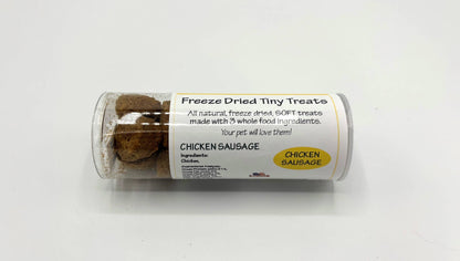 A clear plastic cylinder container of freeze dried tiny treats, labeled 'CHICKEN SAUSAGE' on a white background.