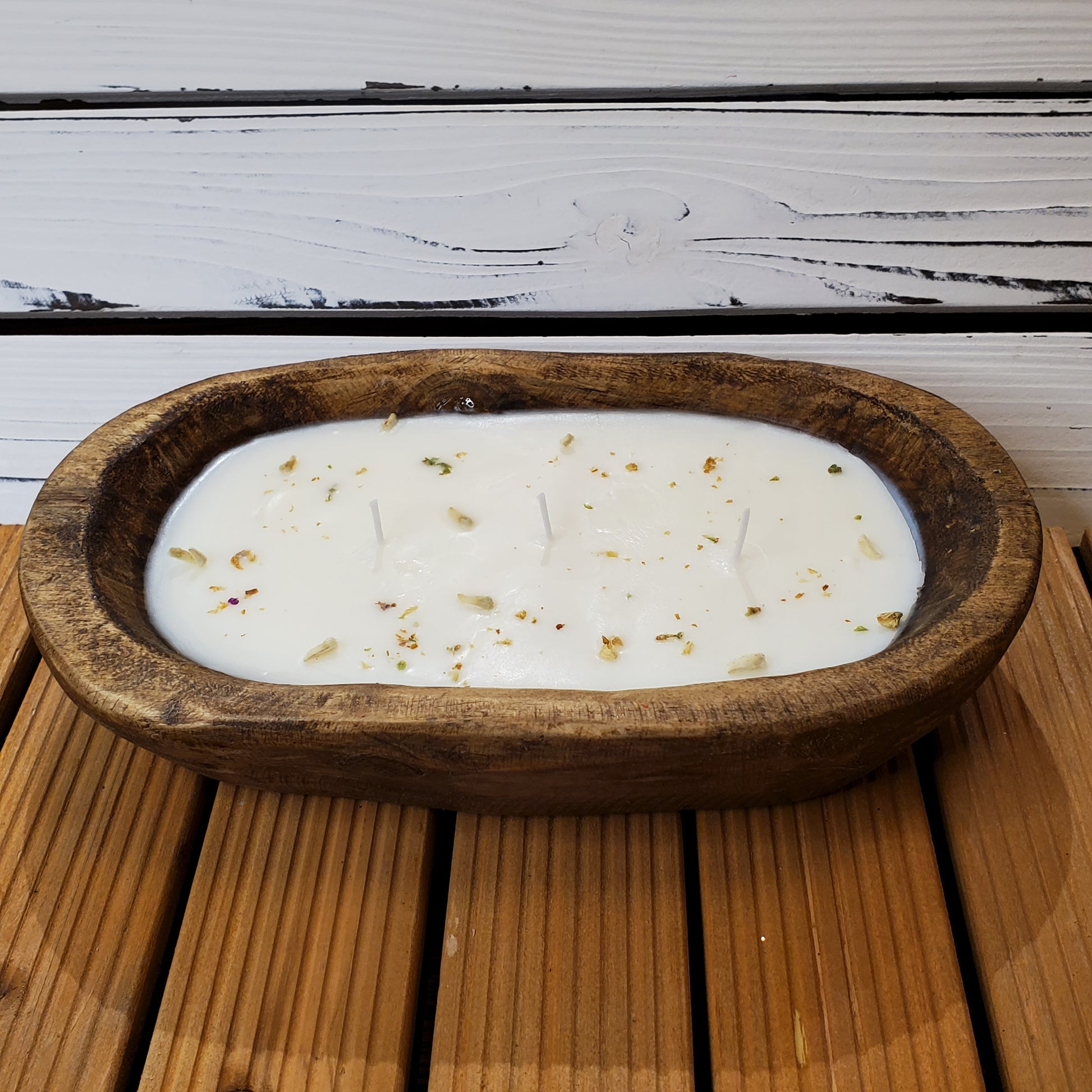 White candle with gold flecks in a wooden bowl on a wooden surface