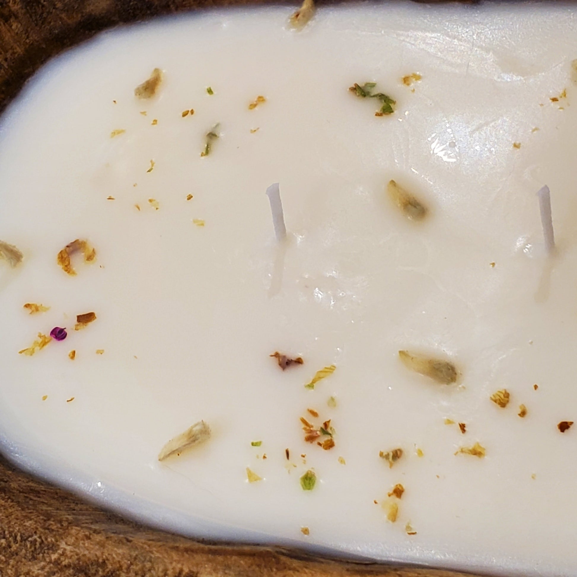 Close-up of a white candle with dried flowers and leaves on top, placed in a wooden holder.