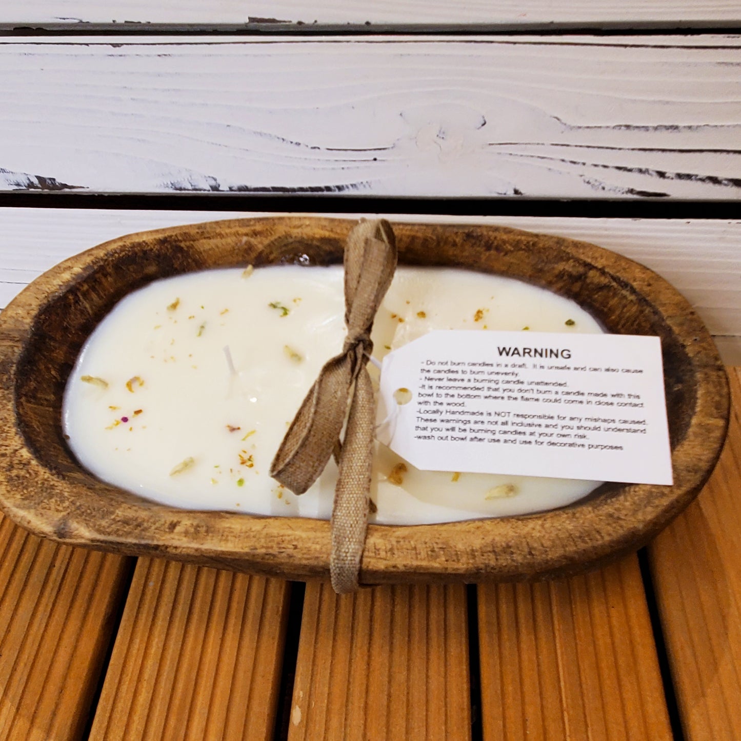 Candle in a wooden dish with a warning label on a wooden surface