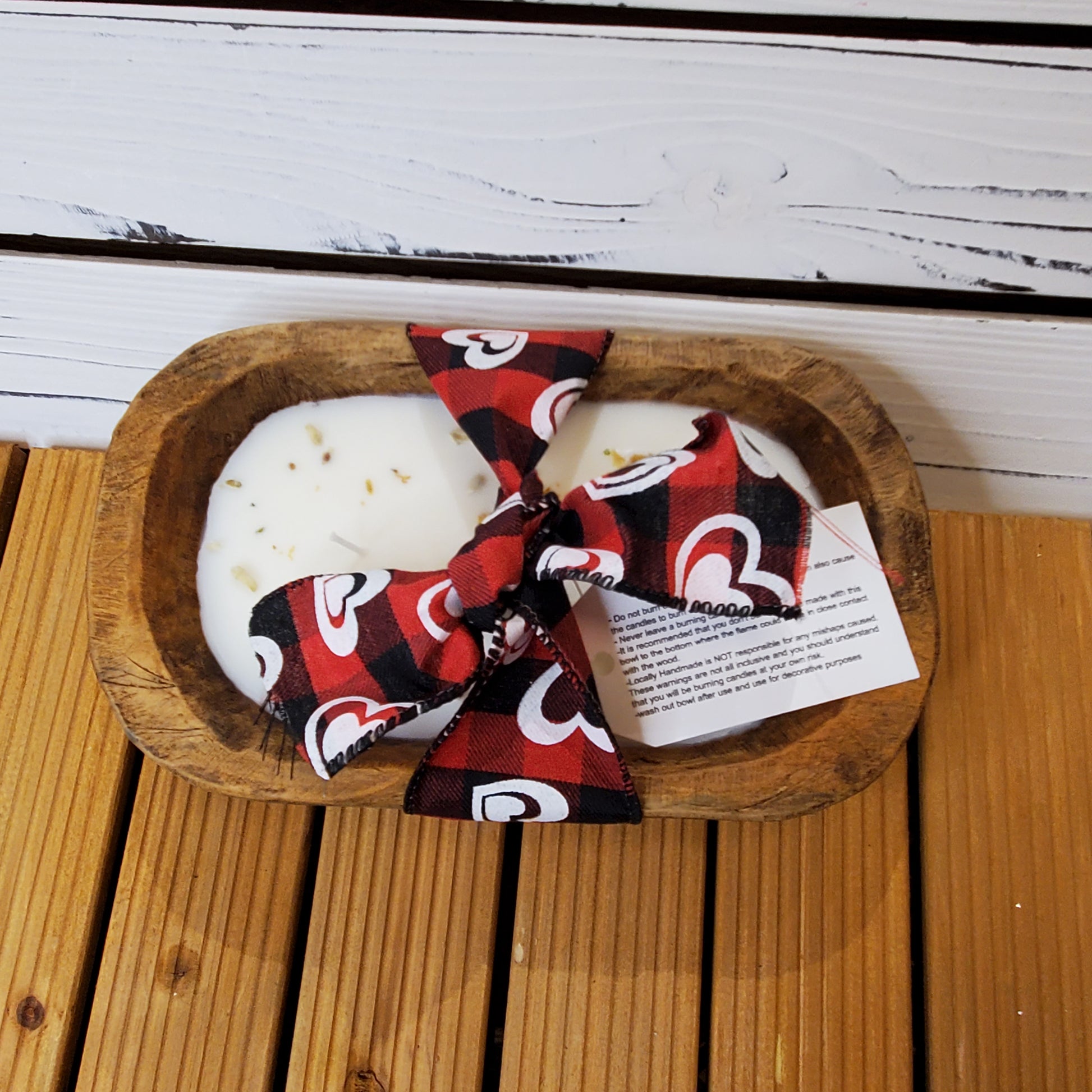 Red and black patterned bow on a white bar of soap in a wooden dish with a white background