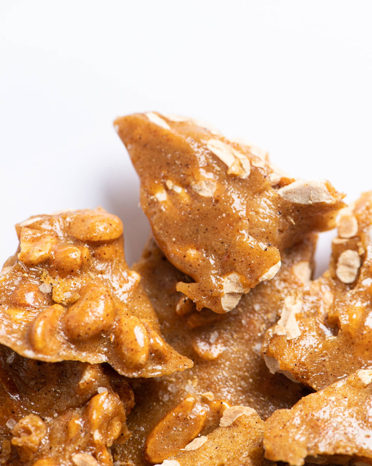 Close-up of caramel-colored brittle candy with visible oats and nuts, set against a clean white background.