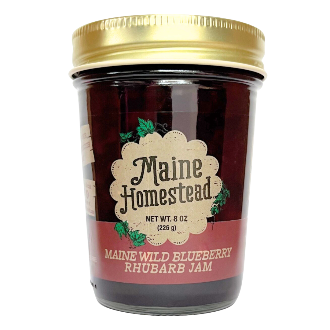 A jar of Maine Homestead Maine Wild Blueberry Rhubarb Jam with a gold metal lid and a cream and red label, set against a plain white background.