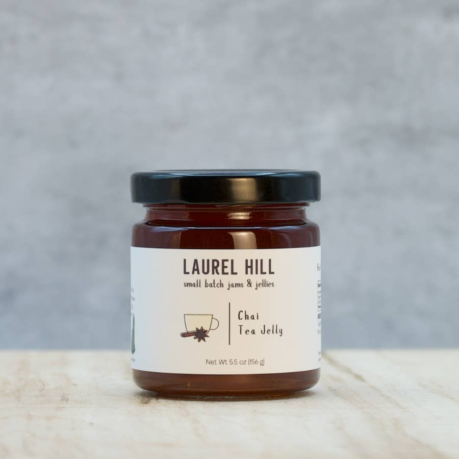 A jar of Laurel Hill Chai Tea Jelly on a light wooden surface against a textured gray background.