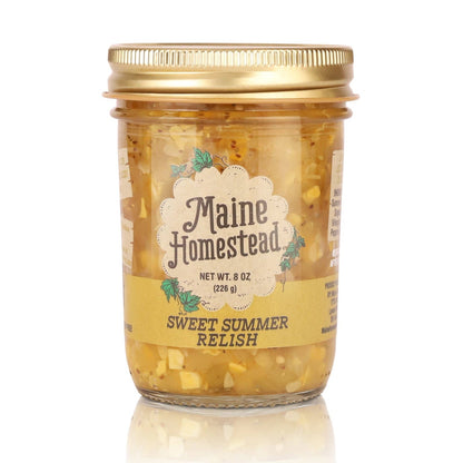 A glass jar of Maine Homestead Sweet Summer Relish with a gold metal lid and a cream-colored label, set against a plain white background with a soft reflection below.