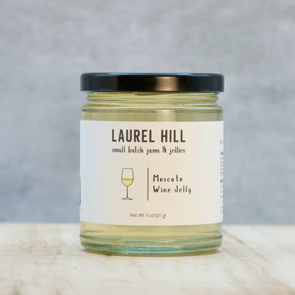 A small glass jar of Laurel Hill Moscato Wine Jelly with a black lid and a cream label, set on a light marble surface against a textured gray background.