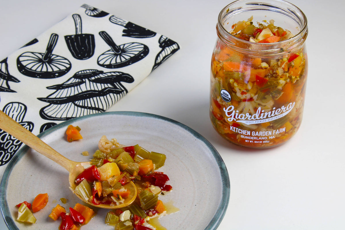 Jar of Giardinieri relish on a plate with a wooden spoon, next to a patterned napkin.