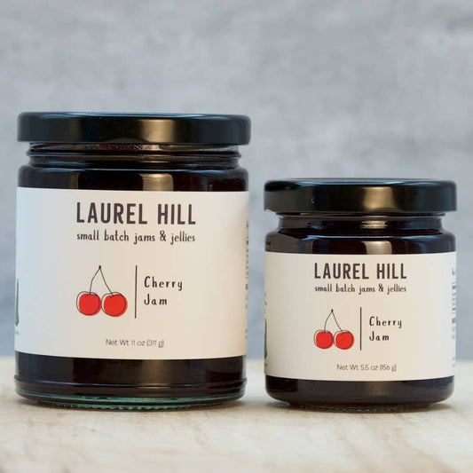 Two jars of Laurel Hill cherry jam on a marble surface with a gray background