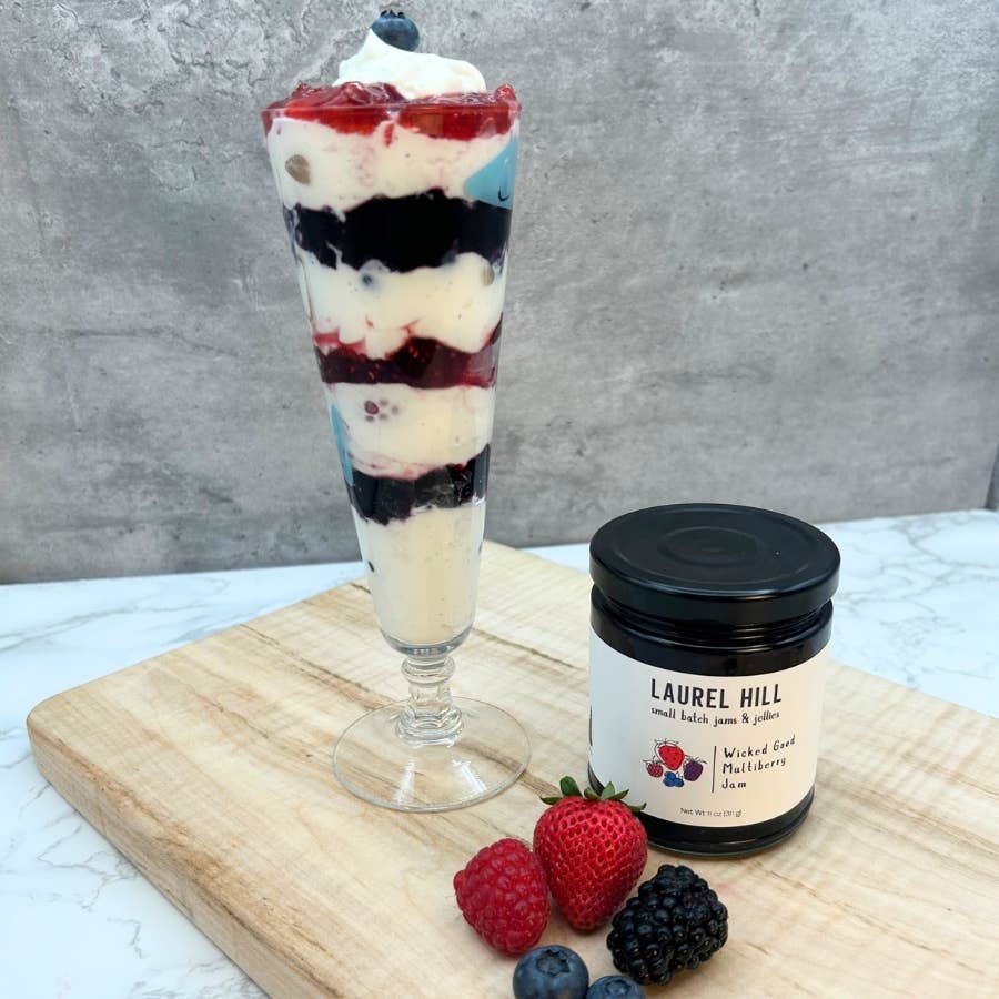 Dessert parfait with berries and a jar of Laurel Hill jam on a wooden board.