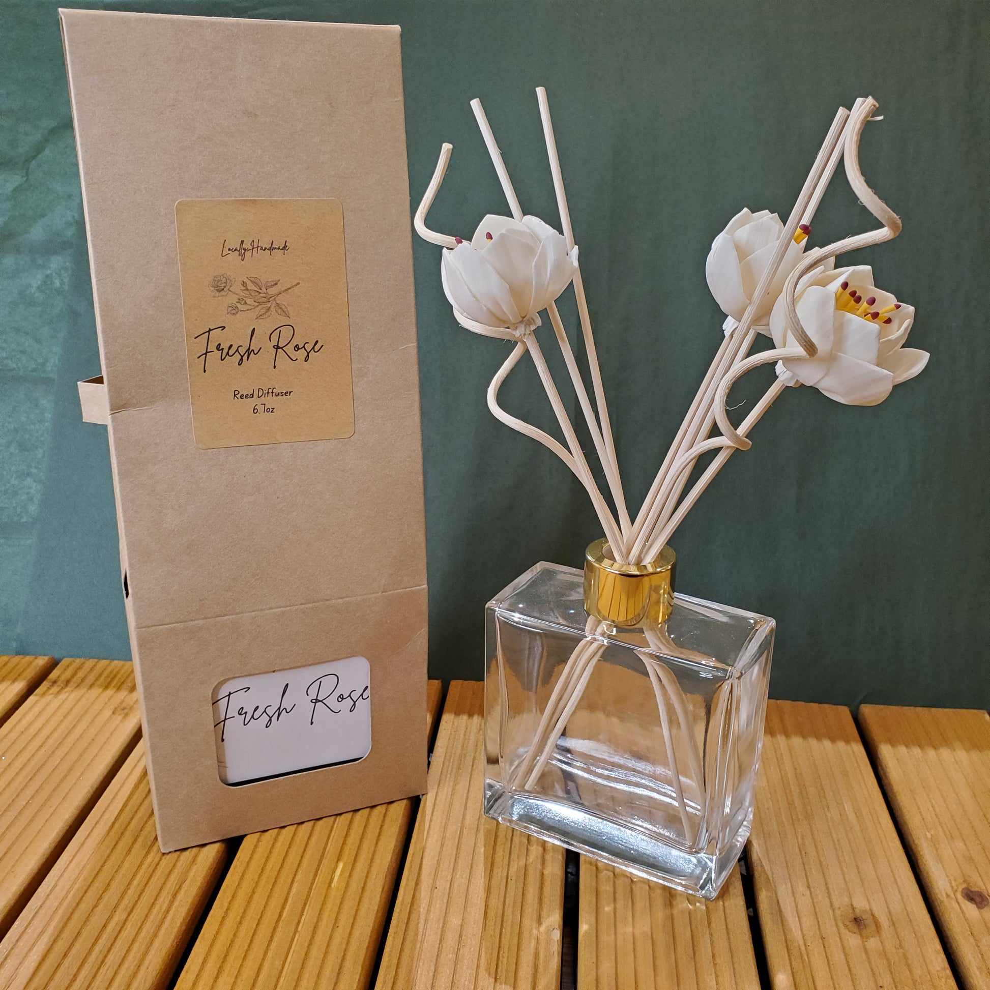 Clear glass diffuser with white floral sticks on a cardboard packaging labeled 'Fresh Rose'.