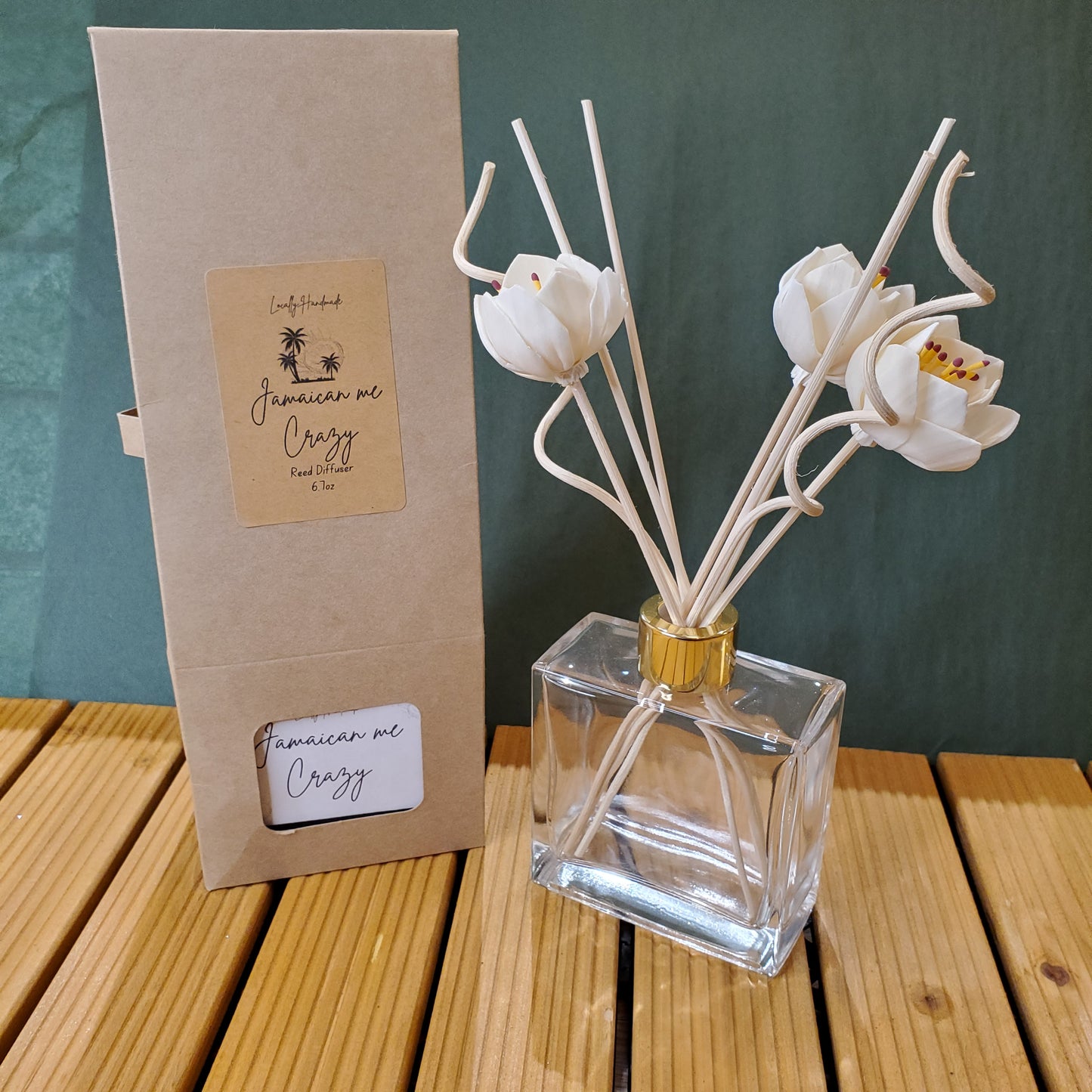 Clear glass perfume bottle with white floral design on a green surface with wooden background