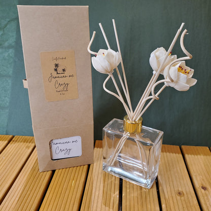 Clear glass perfume bottle with white floral design on a green surface with wooden background