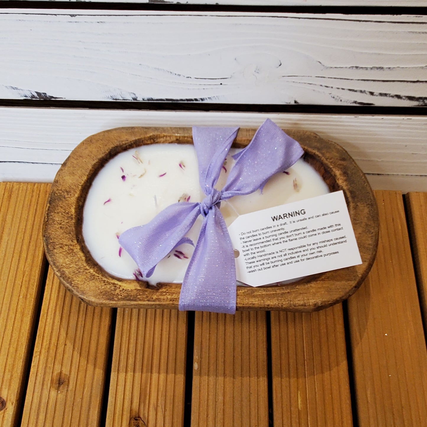 Candle in a wooden dish with a purple ribbon on a wooden surface