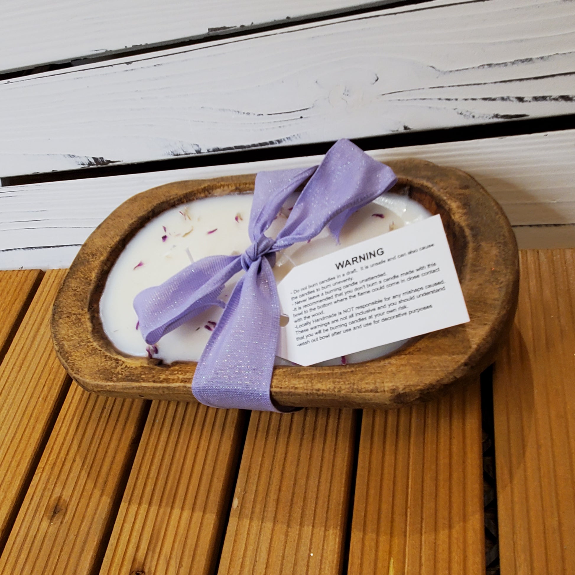 Candle in a wooden dish with a purple ribbon on a wooden surface