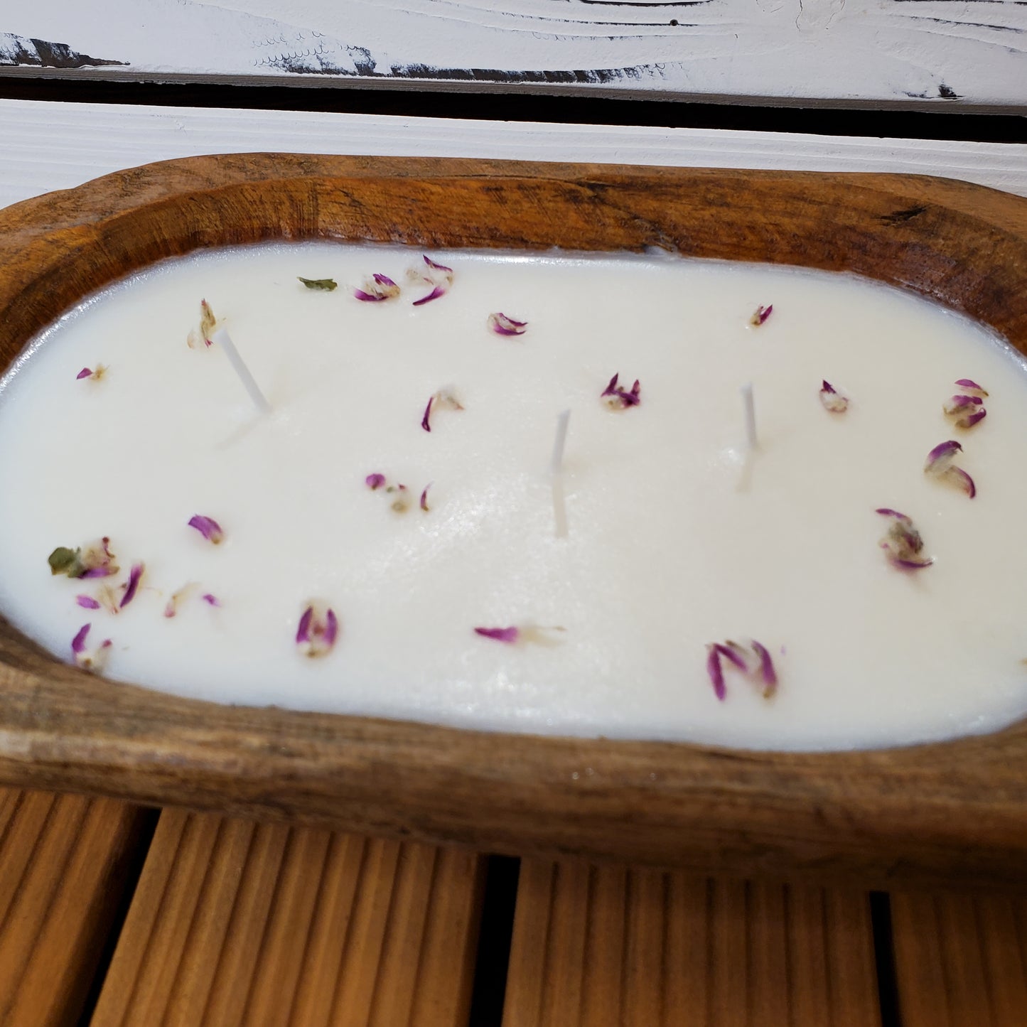Candle with flower petals in a wooden dish on a wooden surface